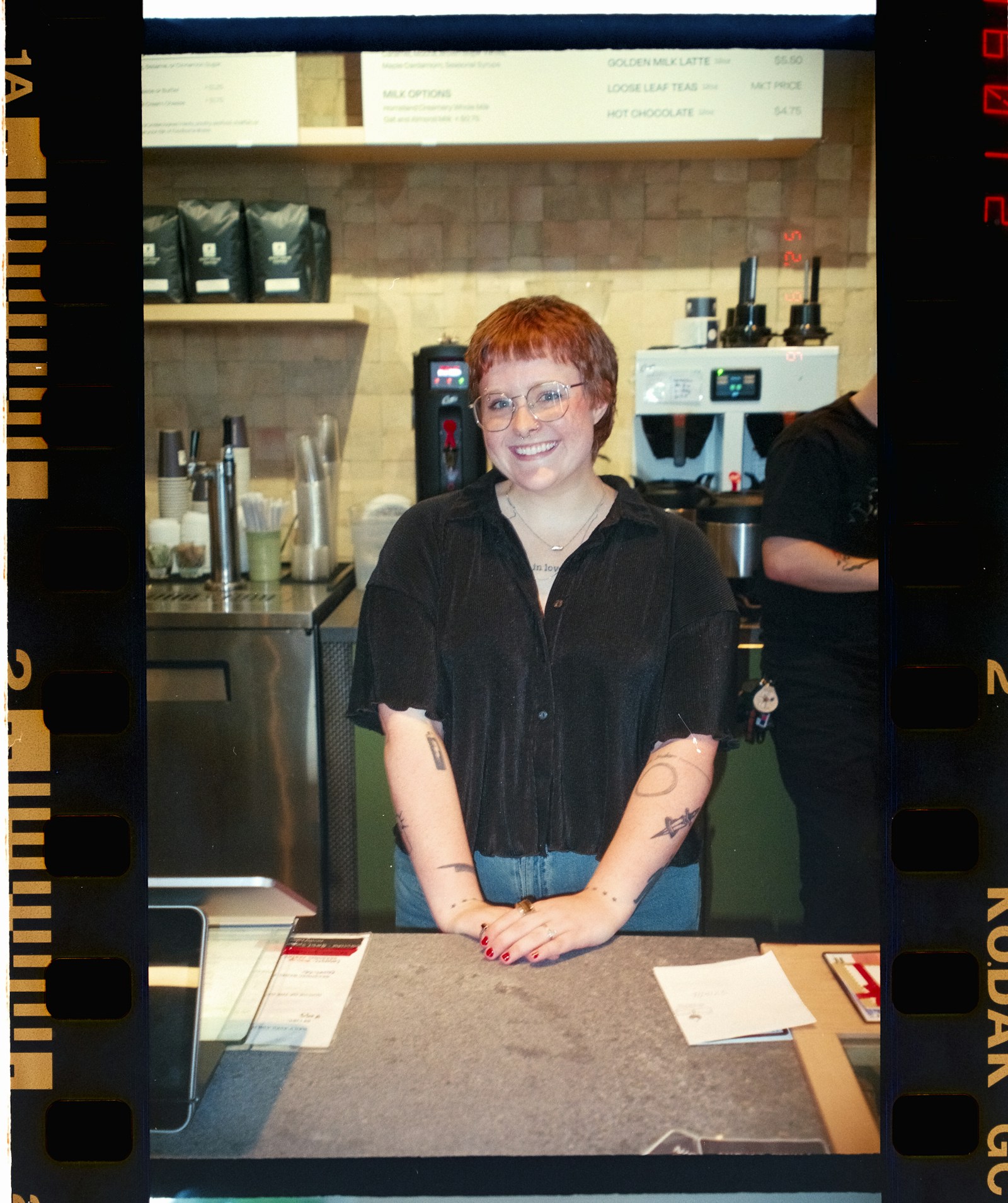 A smiling barista behind the counter of a neighborhood café